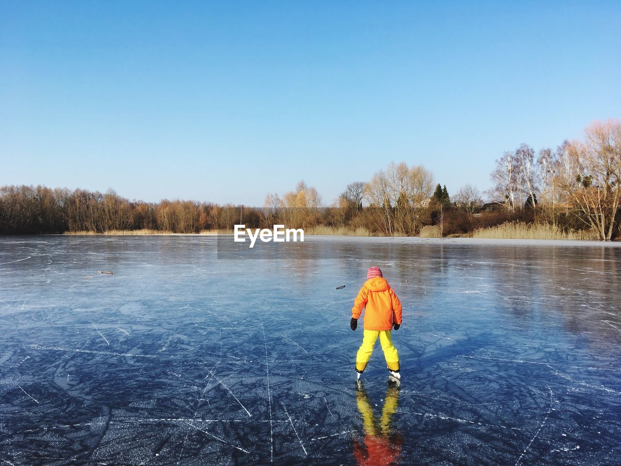 Rear view of child skating on ice rink against clear sky