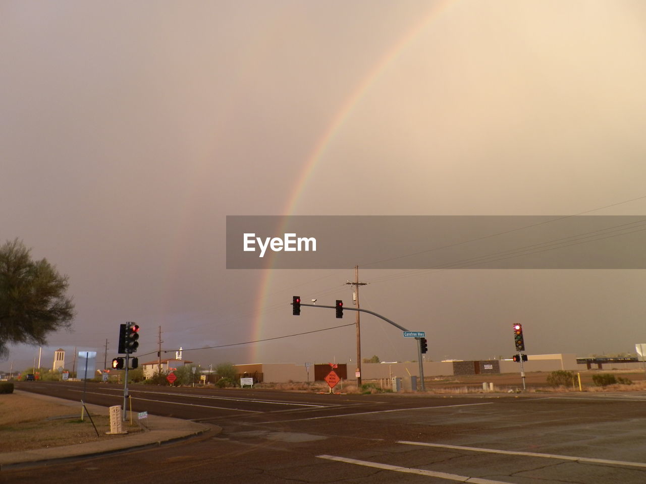 rainbow, sky, road, nature, transportation, architecture, city, beauty in nature, street, storm, cloud, no people, rain, wet, sign, environment, building exterior, outdoors, built structure, mode of transportation, tree, car, scenics - nature, motor vehicle, dramatic sky