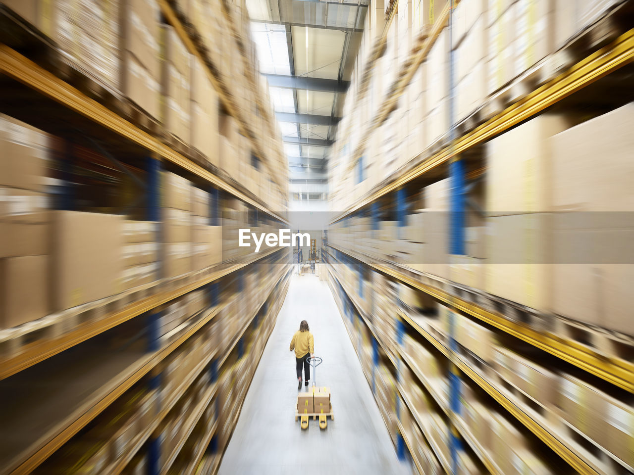 Warehouse worker pulling pallet jack walking in alley amidst racks