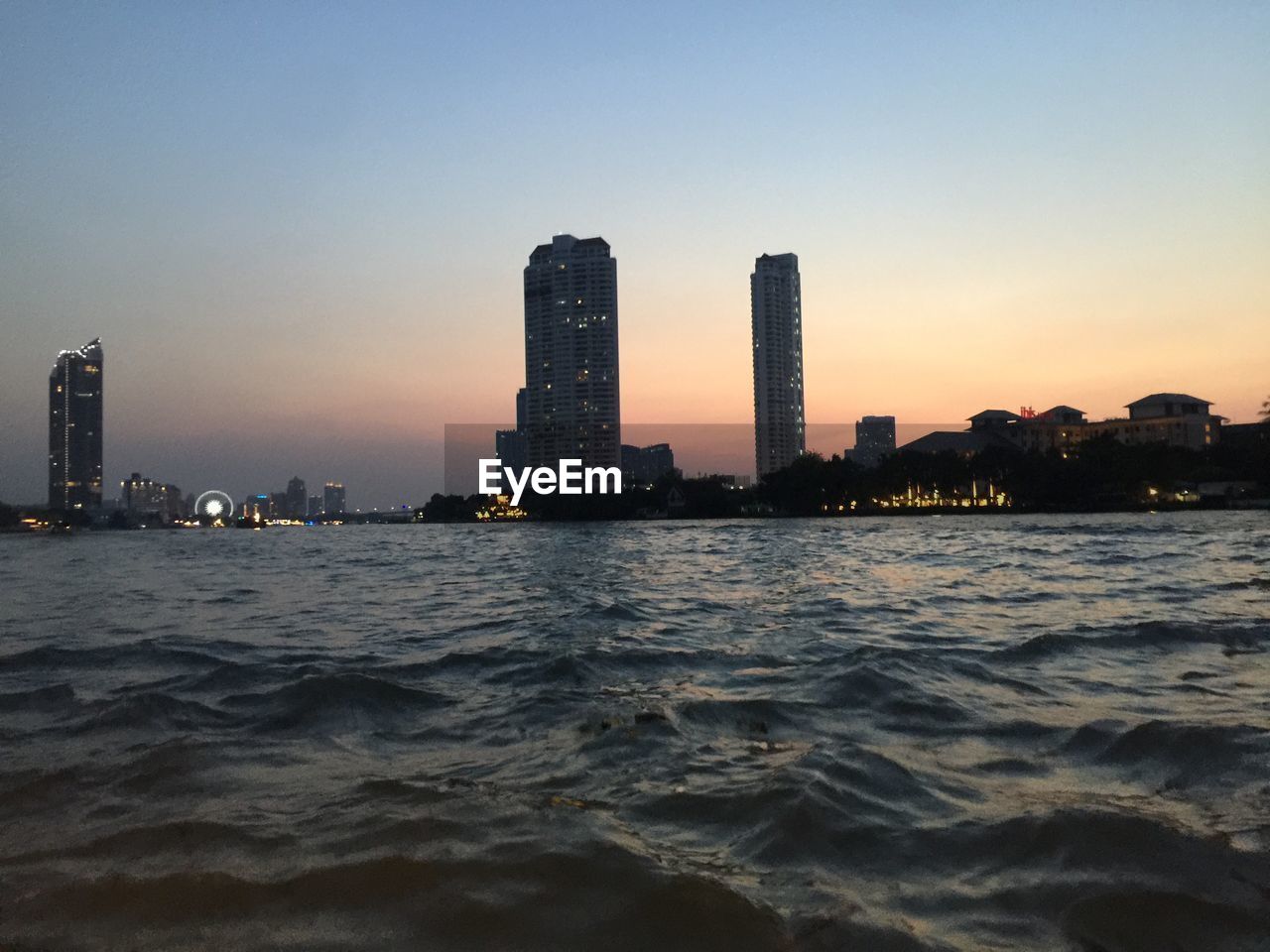 SEA BY BUILDINGS AGAINST CLEAR SKY DURING SUNSET