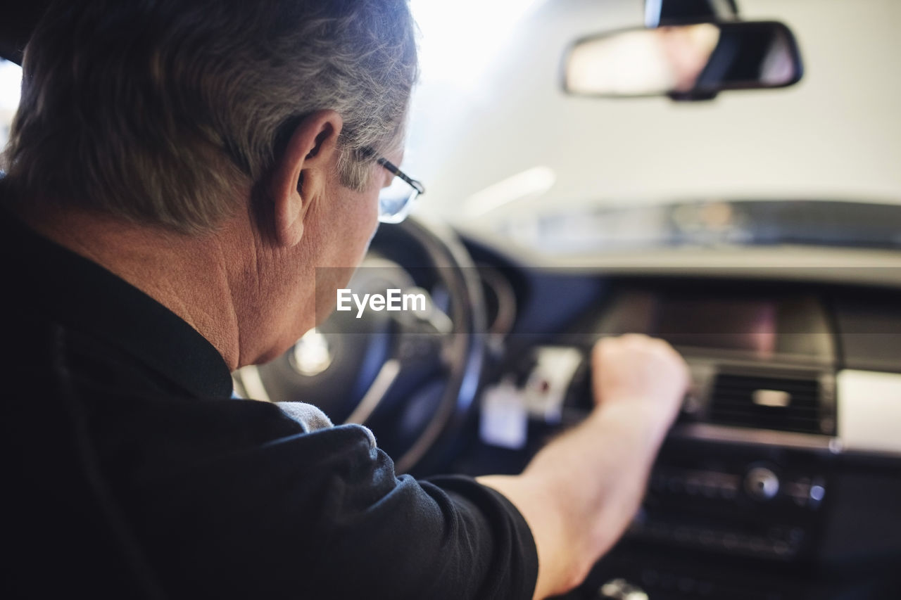 Close-up of senior mechanic examining air conditioner while sitting in car