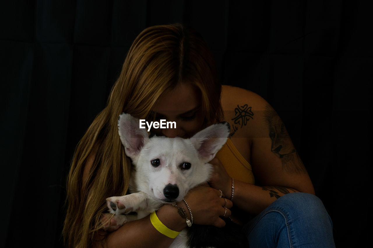 Woman kissing dog against black background