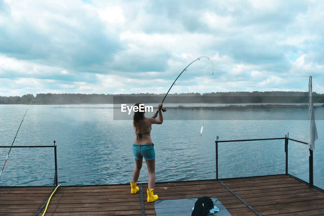 Rear view of woman fishing in river against sky