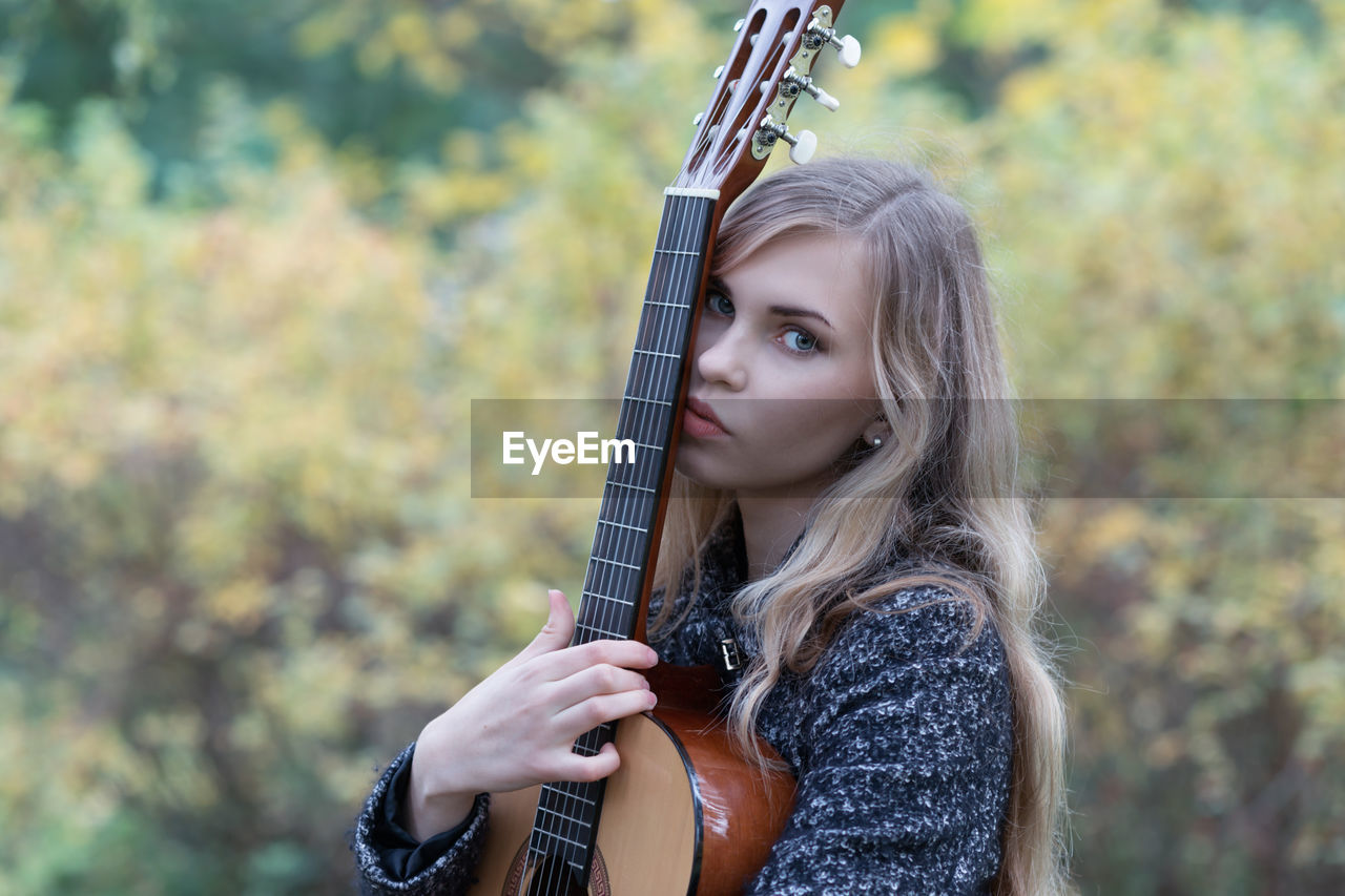 Portrait of beautiful young woman holding guitar outdoors