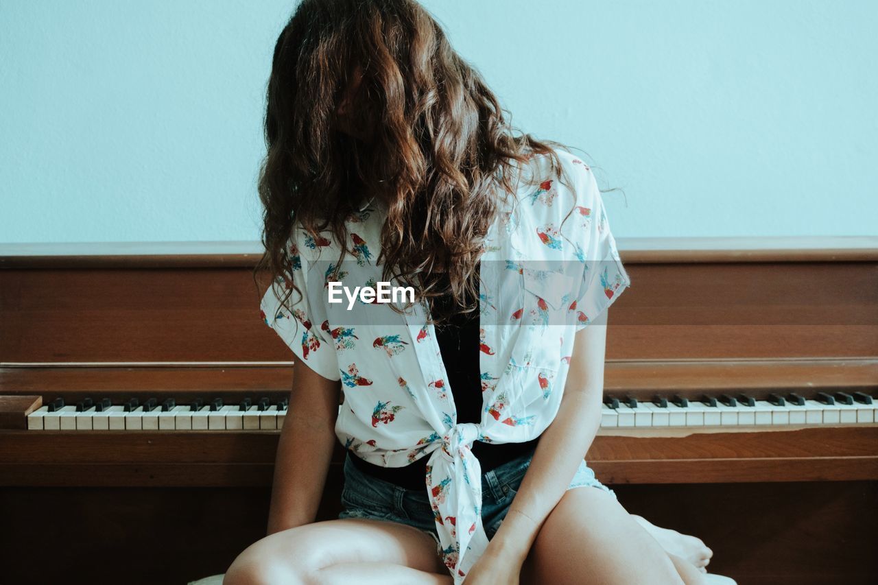 Woman with tangled hair sitting by piano at home