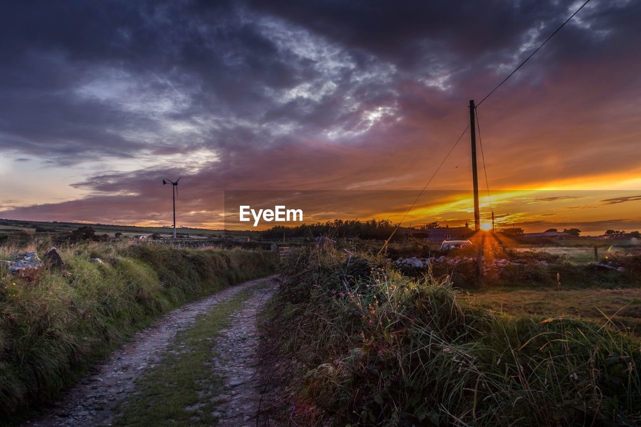 Road amidst field against dramatic sky during sunset