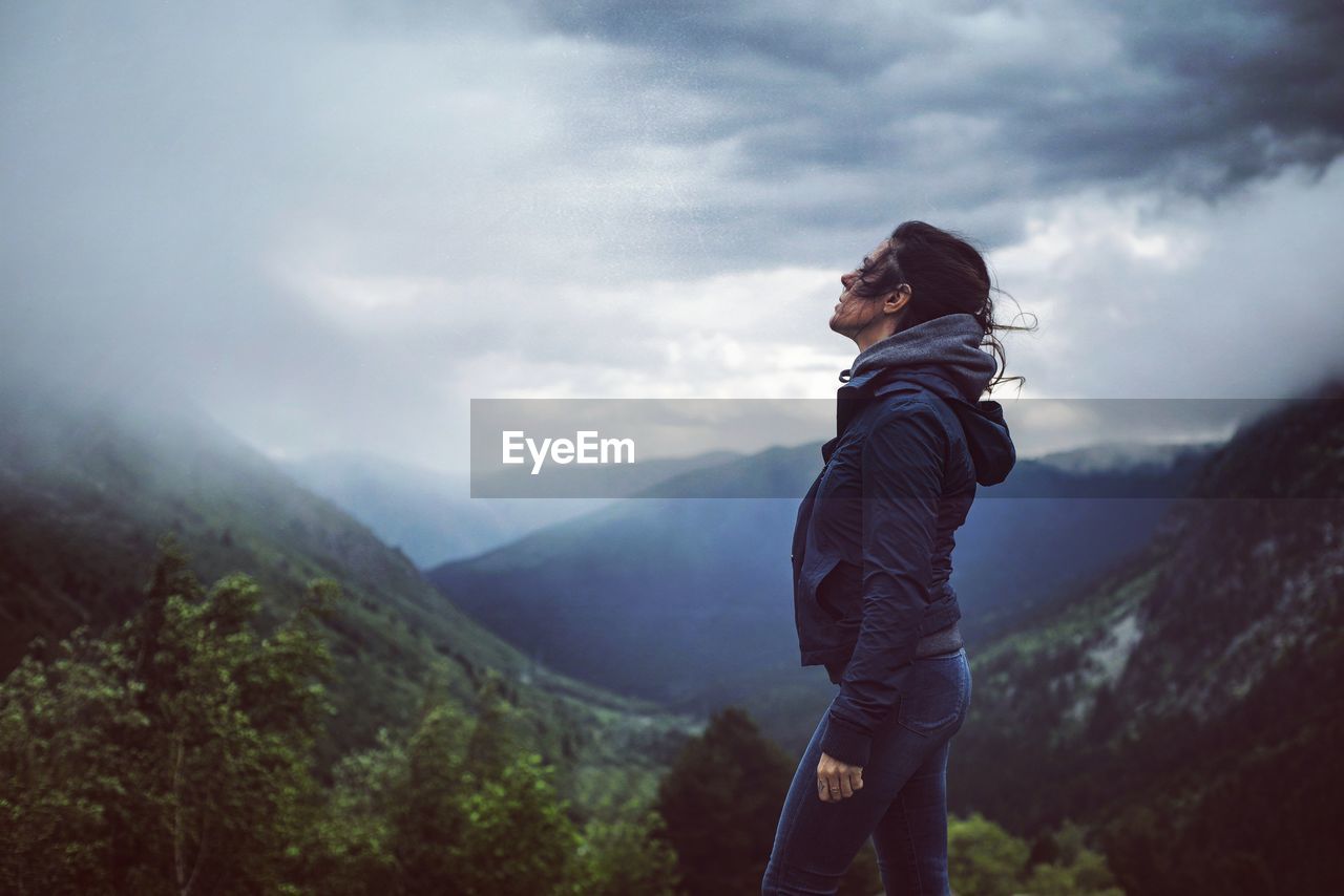 Side view of man standing on mountain against cloudy sky