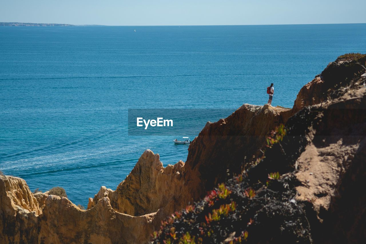 Mid distance view of woman standing on cliff by sea