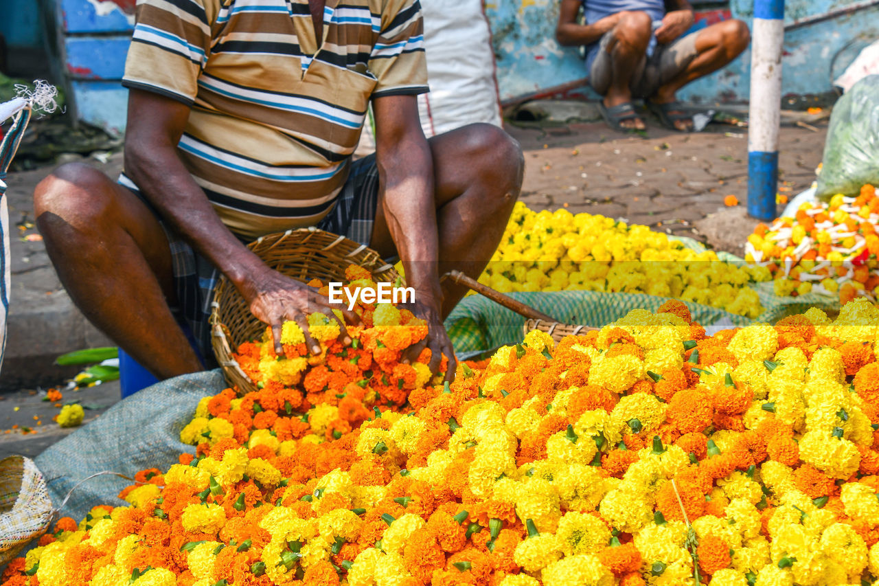 MIDSECTION OF PERSON HOLDING FLOWERS AT MARKET