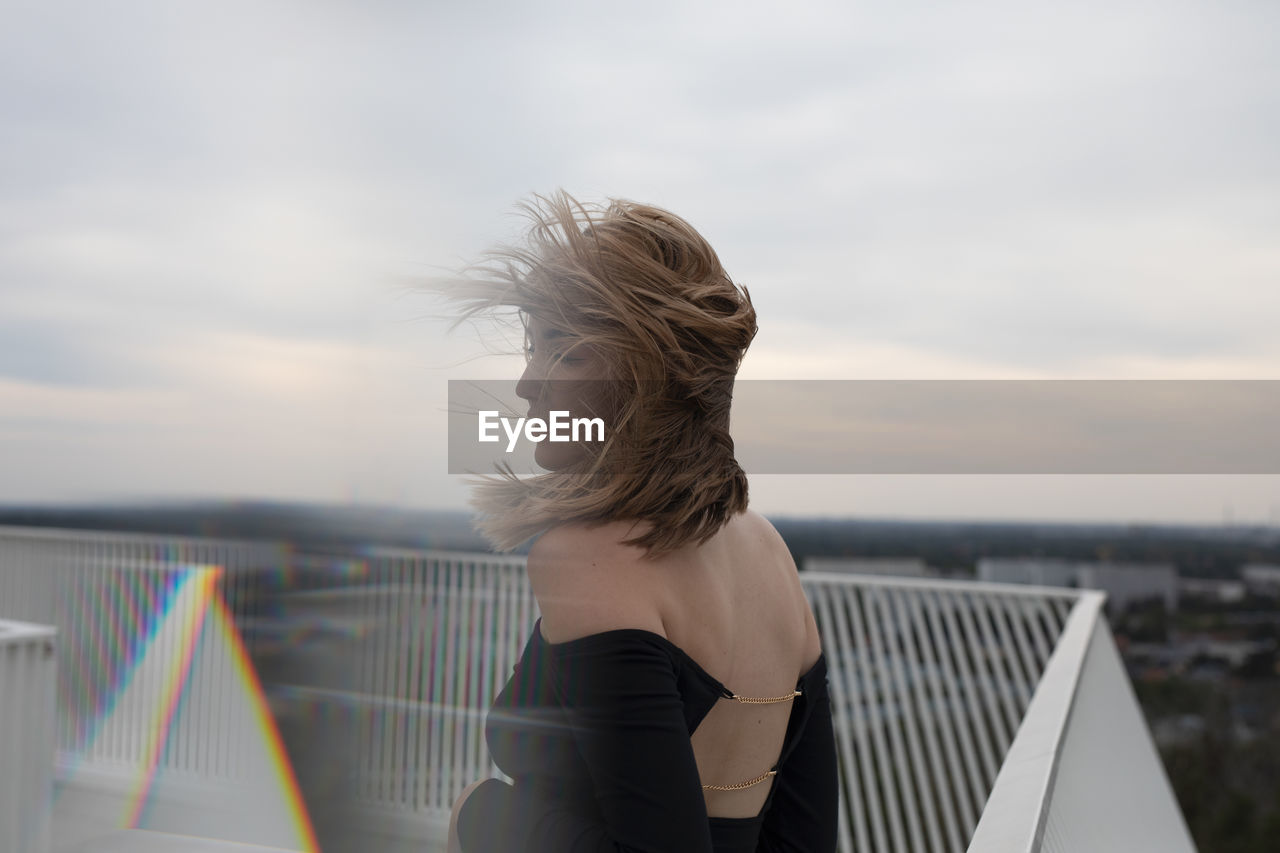 Rear view of woman standing by railing against sky