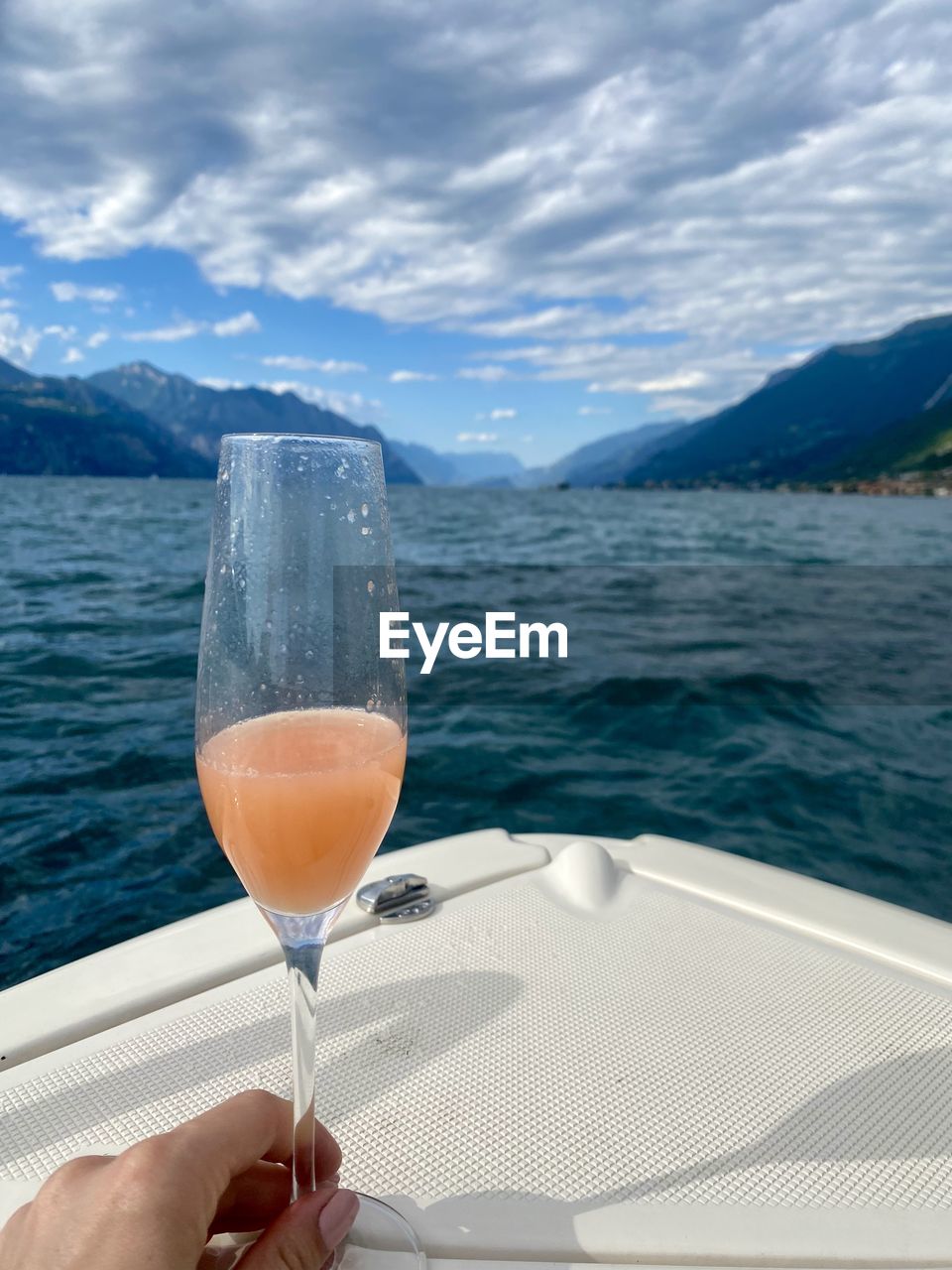 refreshment, water, alcohol, drink, sky, food and drink, nature, wine, cloud, glass, mountain, sea, vacation, travel, trip, scenics - nature, leisure activity, holiday, hand, one person, beauty in nature, adult, wine glass, transportation, household equipment, drinking glass, lifestyles, land, luxury, nautical vessel, personal perspective, day, outdoors, mountain range, travel destinations, champagne, summer, relaxation, mode of transportation, holding, food, freshness, beach, champagne flute, sunlight, women, wealth, vehicle
