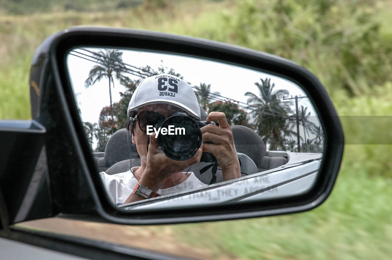 Close-up of mature woman photographing with camera reflecting on side-view mirror