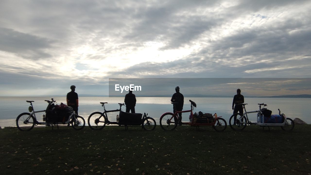 PEOPLE RIDING BICYCLES ON SHORE AGAINST SKY