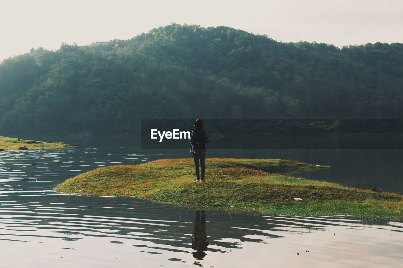 Woman standing at lakeshore against mountains