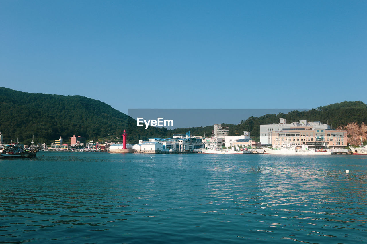 Scenic view of sea by buildings against clear blue sky