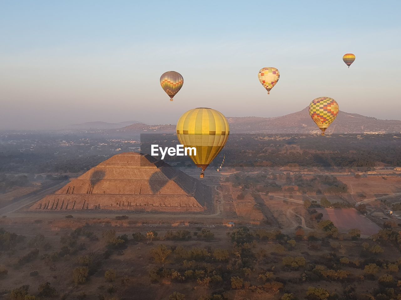 Hot air balloons flying over landscape and ancient pyramid