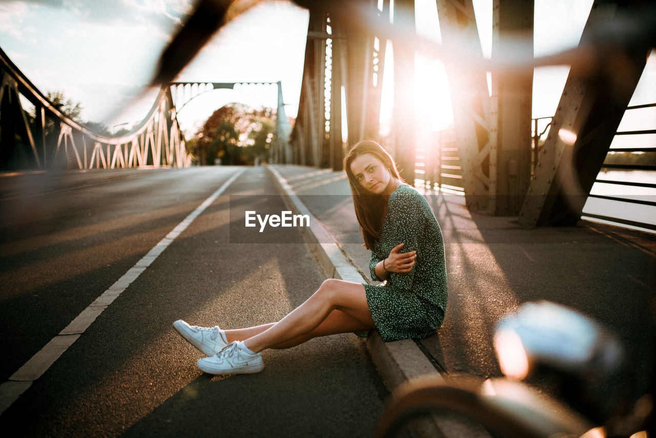 YOUNG WOMAN SITTING ON BRIDGE OVER PEOPLE