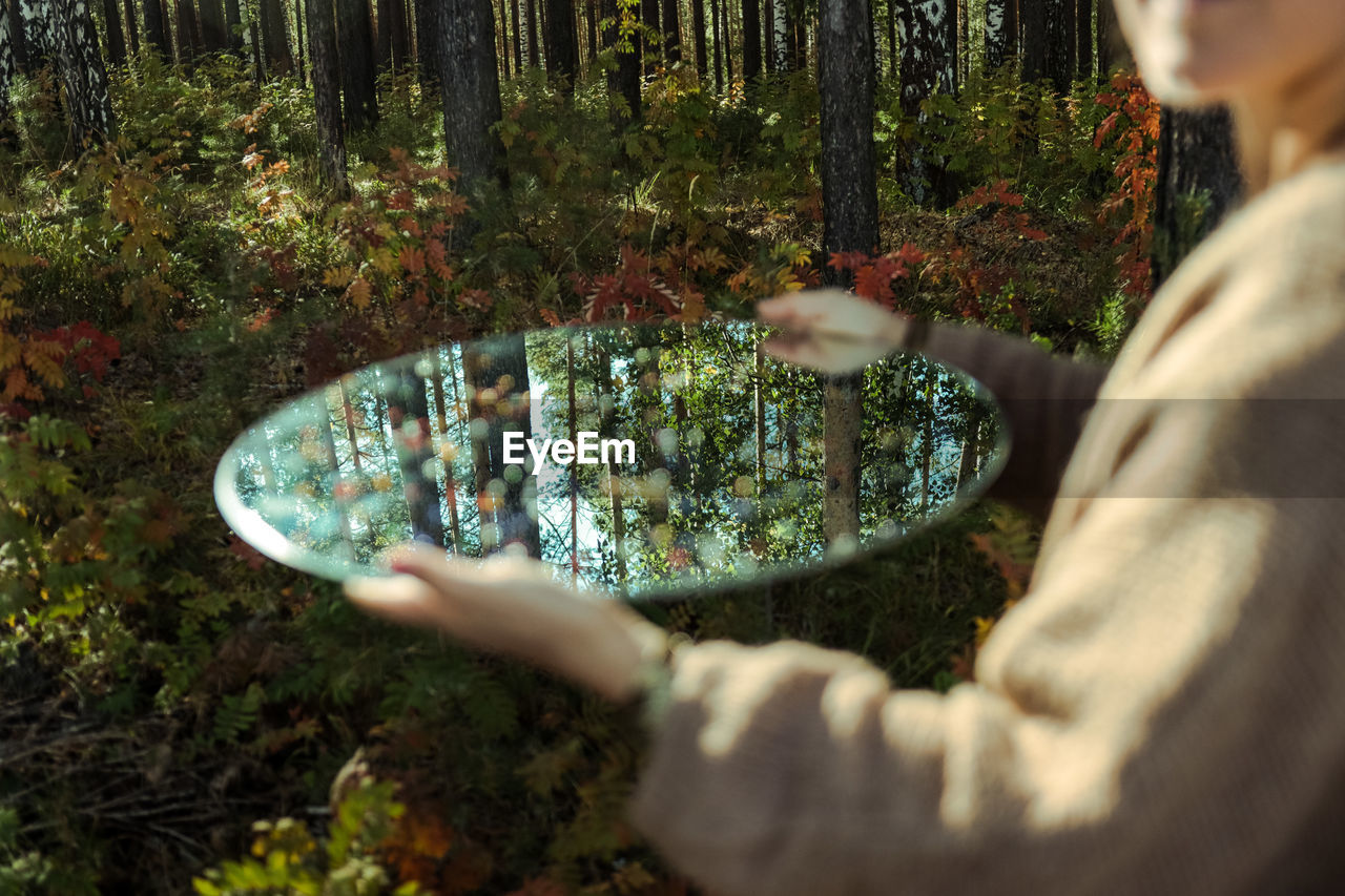 Midsection of woman holding mirror in forest