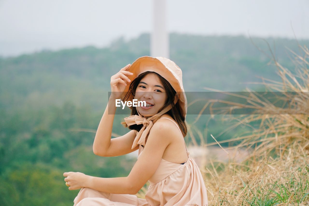 PORTRAIT OF SMILING YOUNG WOMAN STANDING IN FIELD