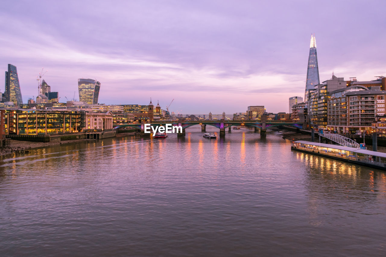 VIEW OF BRIDGE OVER RIVER AGAINST BUILDINGS AT DUSK