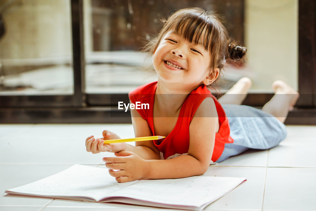 Portrait of girl lying with book on floor