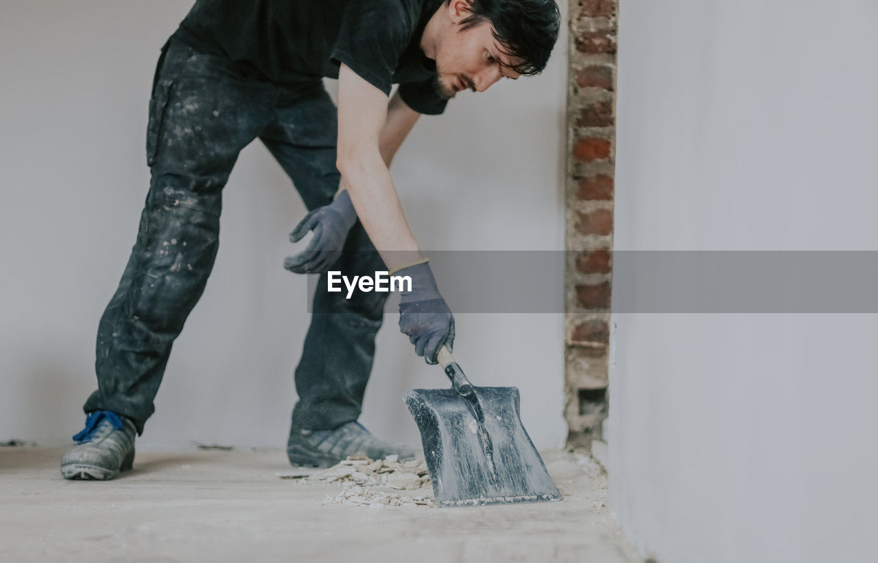 A young man collects construction waste with a dustpan. person