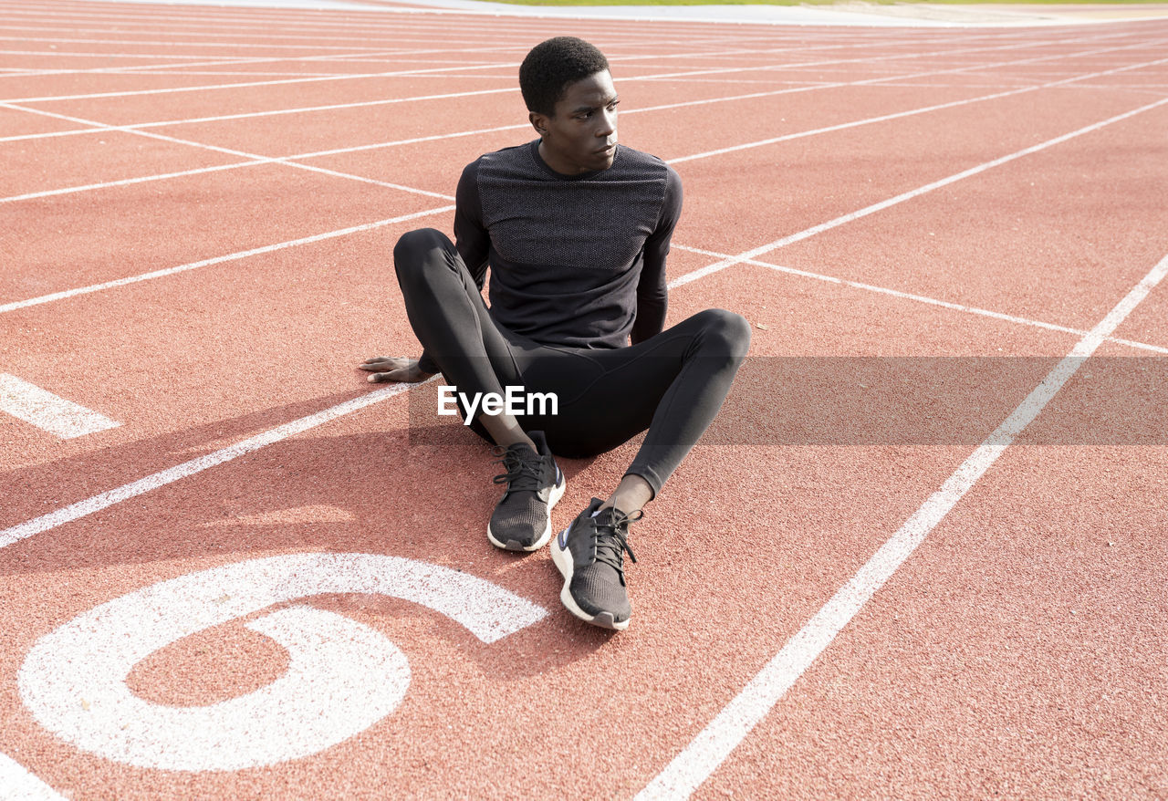 Sportsman contemplating while sitting on running track during sunny day