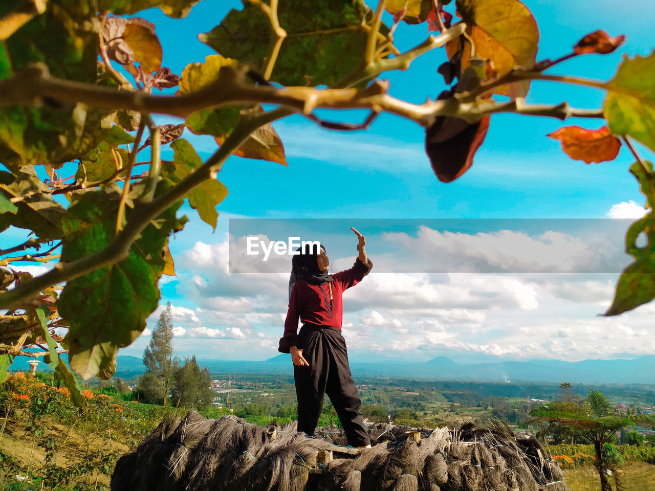 Woman shielding eyes while standing against landscape