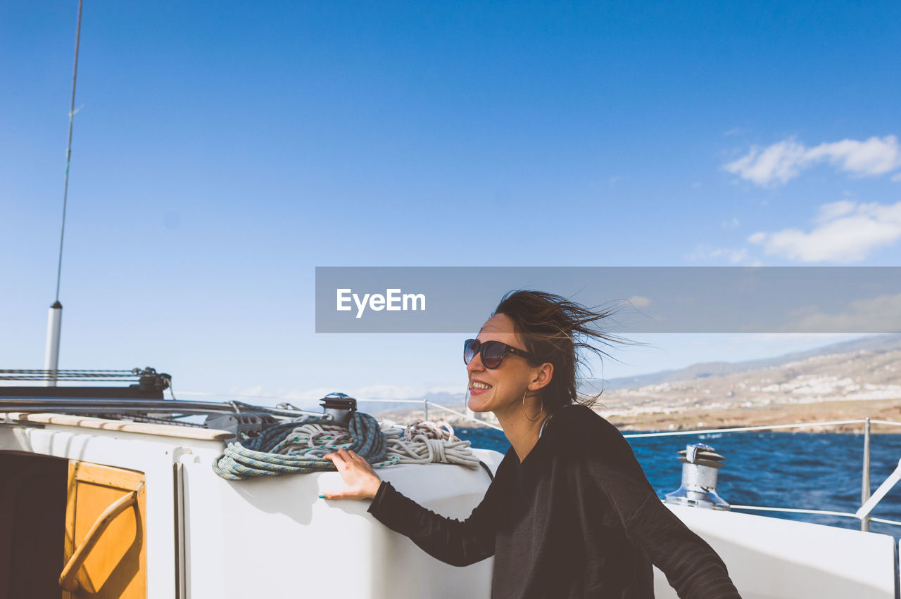 Happy woman with sunglasses on boat in sea against sky