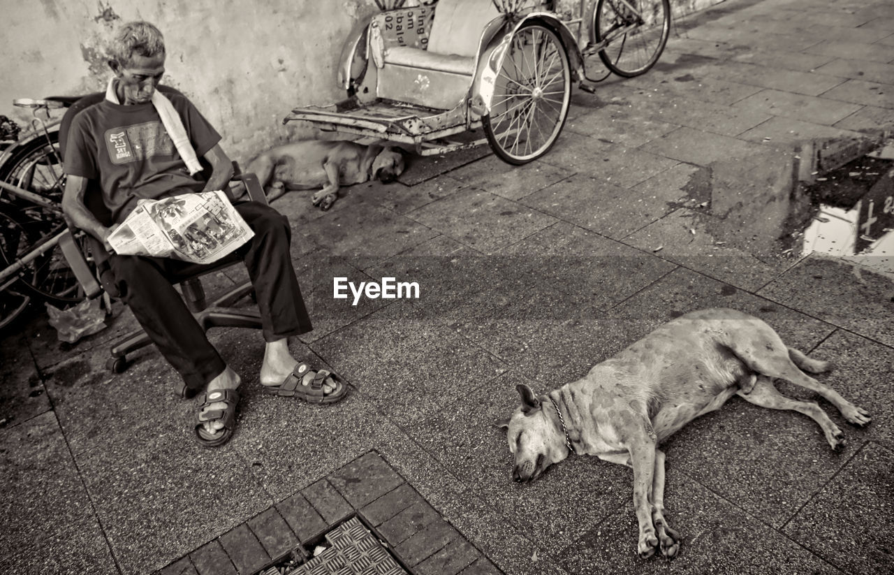 MAN WITH DOG RELAXING ON FOOTPATH