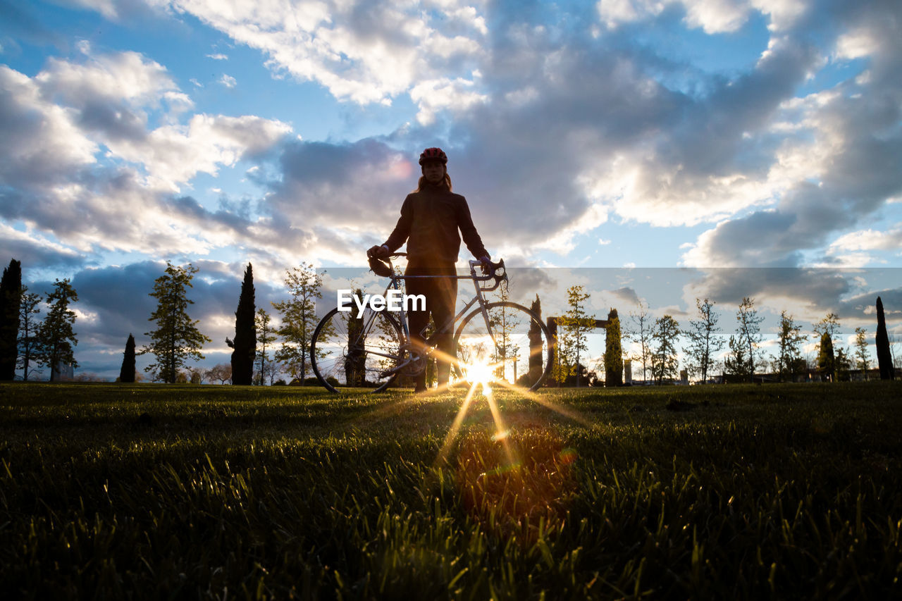 MAN RIDING BICYCLE ON FIELD DURING SUNSET