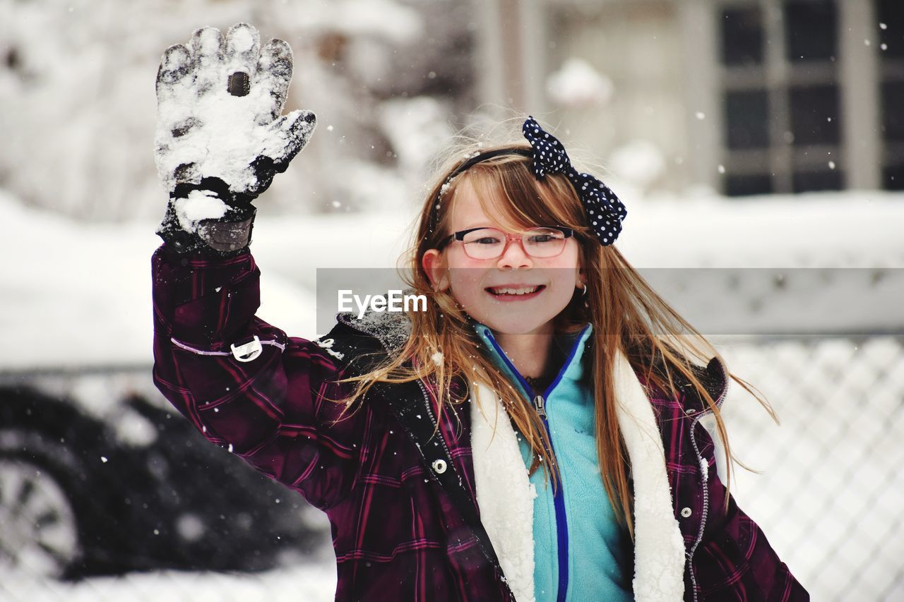 Portrait of smiling girl waving hand during snowfall