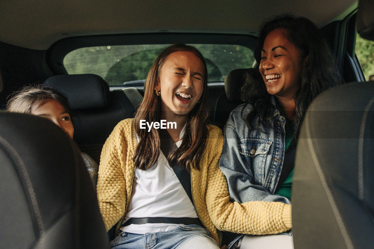 Girl laughing while sitting with mother and sister in car during road trip