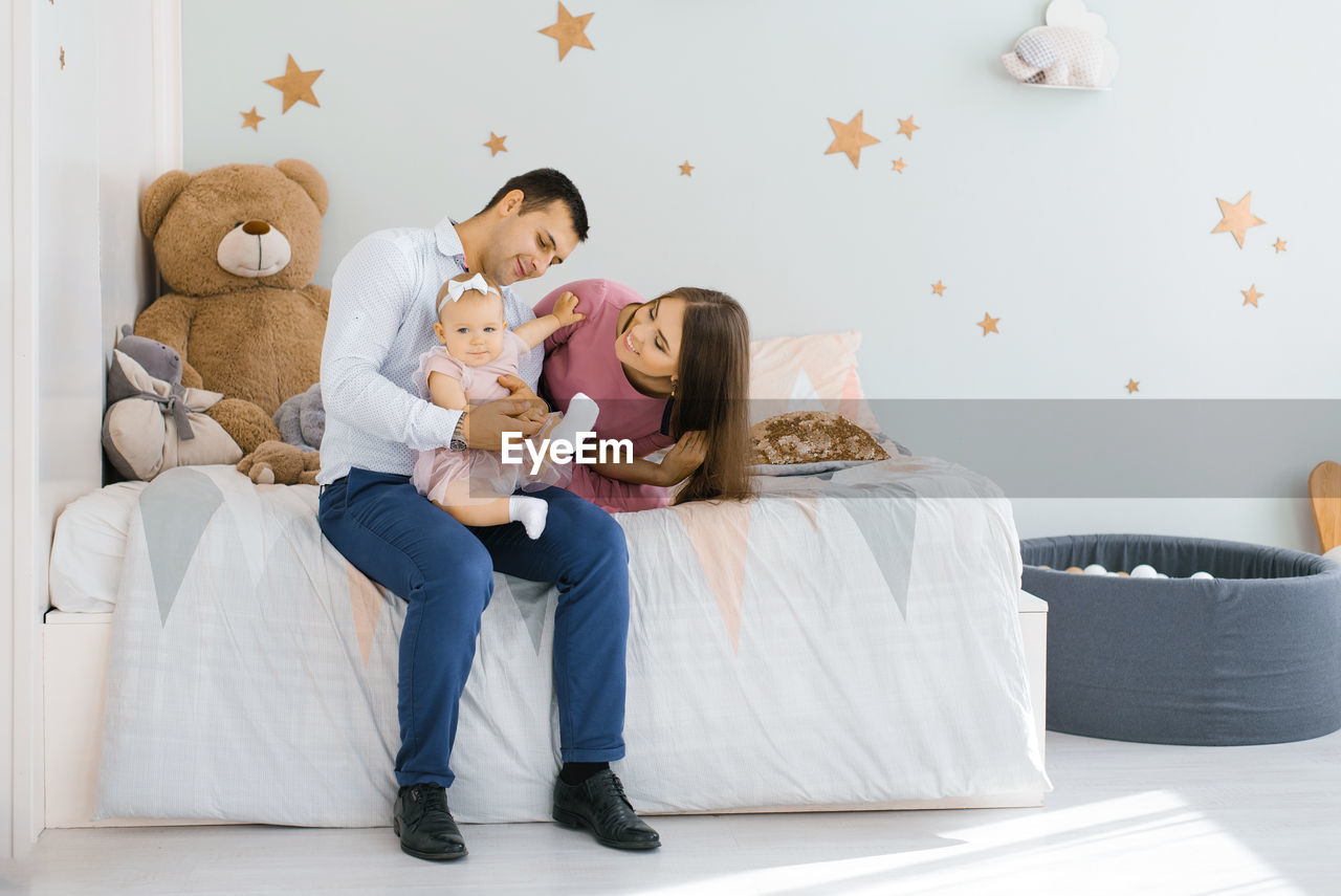 Happy young family sitting on the bed in the children's room and chatting with their  daughter