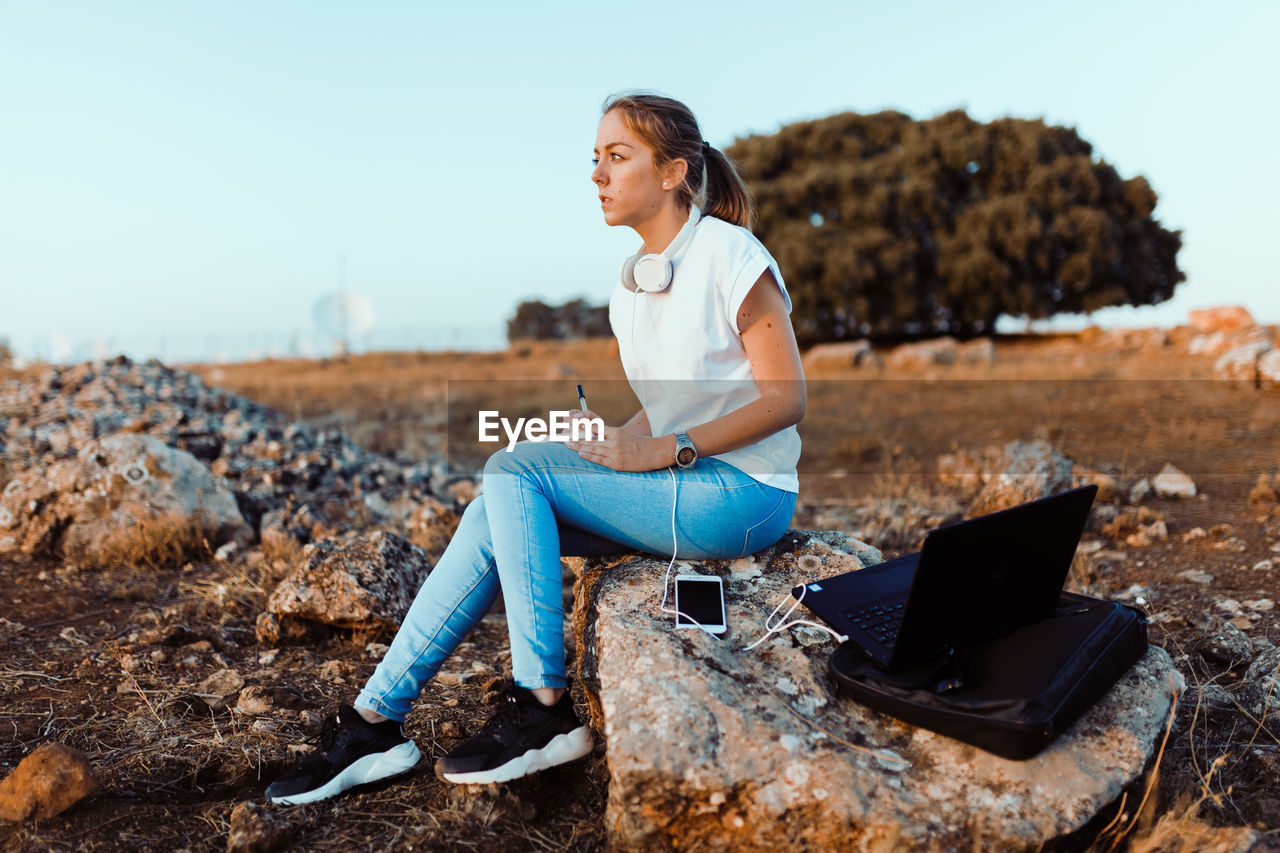 FULL LENGTH OF YOUNG WOMAN SITTING ON ROCKS