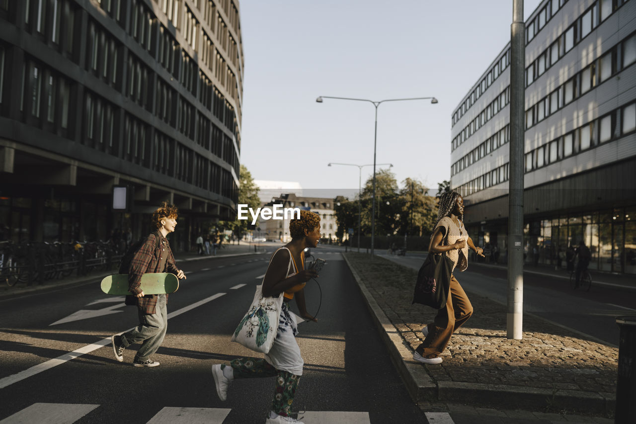 Happy multiracial friends running while crossing street in city