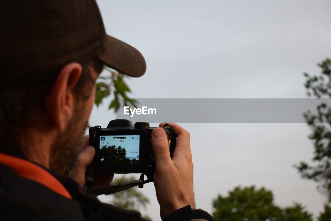 Rear view of man photographing through camera against sky