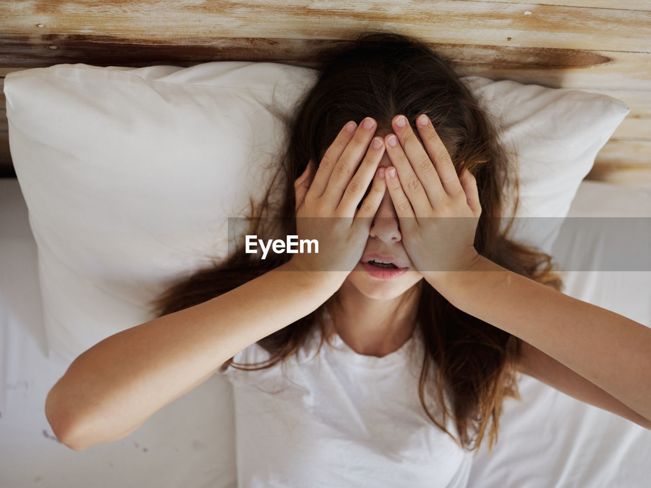 Portrait of woman covering face on bed