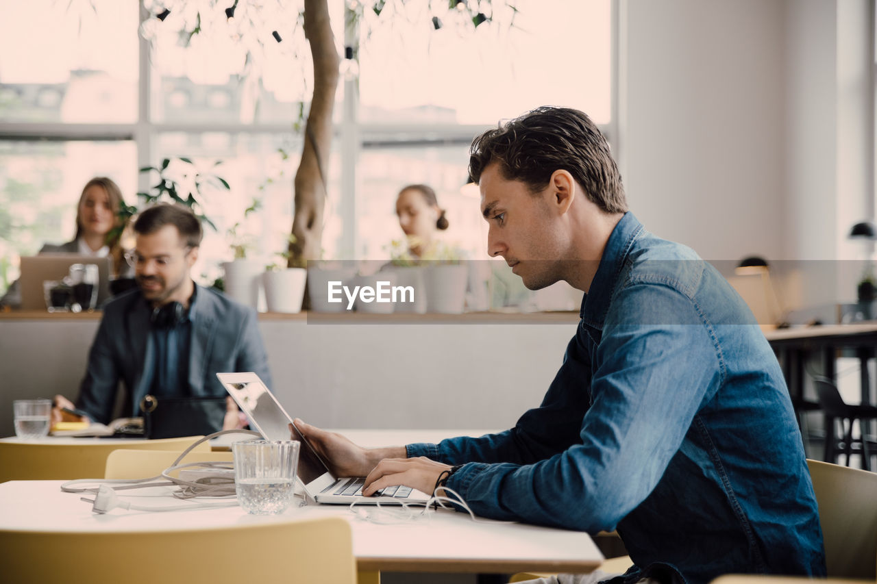 Side view of young businessman using laptop while sitting at desk in coworking space