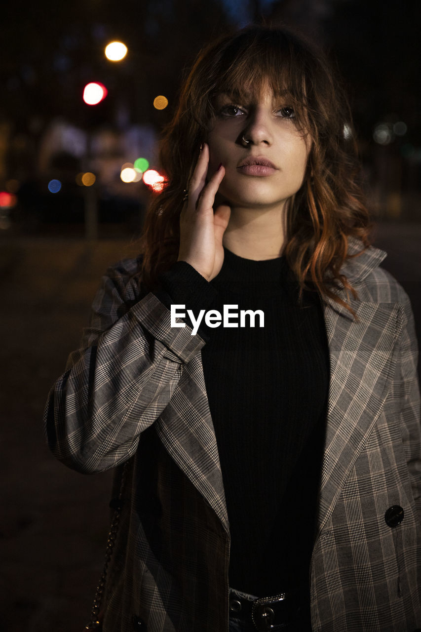 PORTRAIT OF YOUNG WOMAN STANDING AGAINST ILLUMINATED STAR SHAPE AT NIGHT