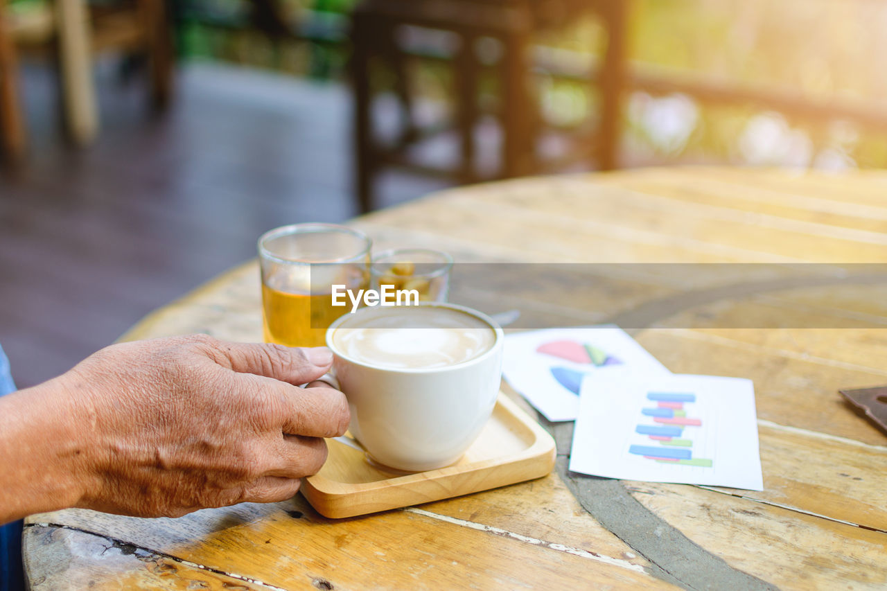 Cropped hands of man holding coffee cup on table at cafe