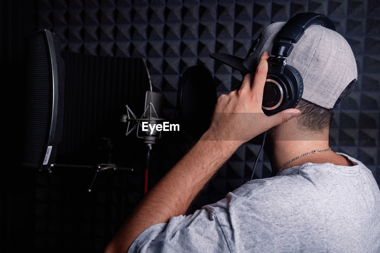 Side view of anonymous male singer in headphones standing in acoustic room with soundproof walls and microphone and recording song in studio