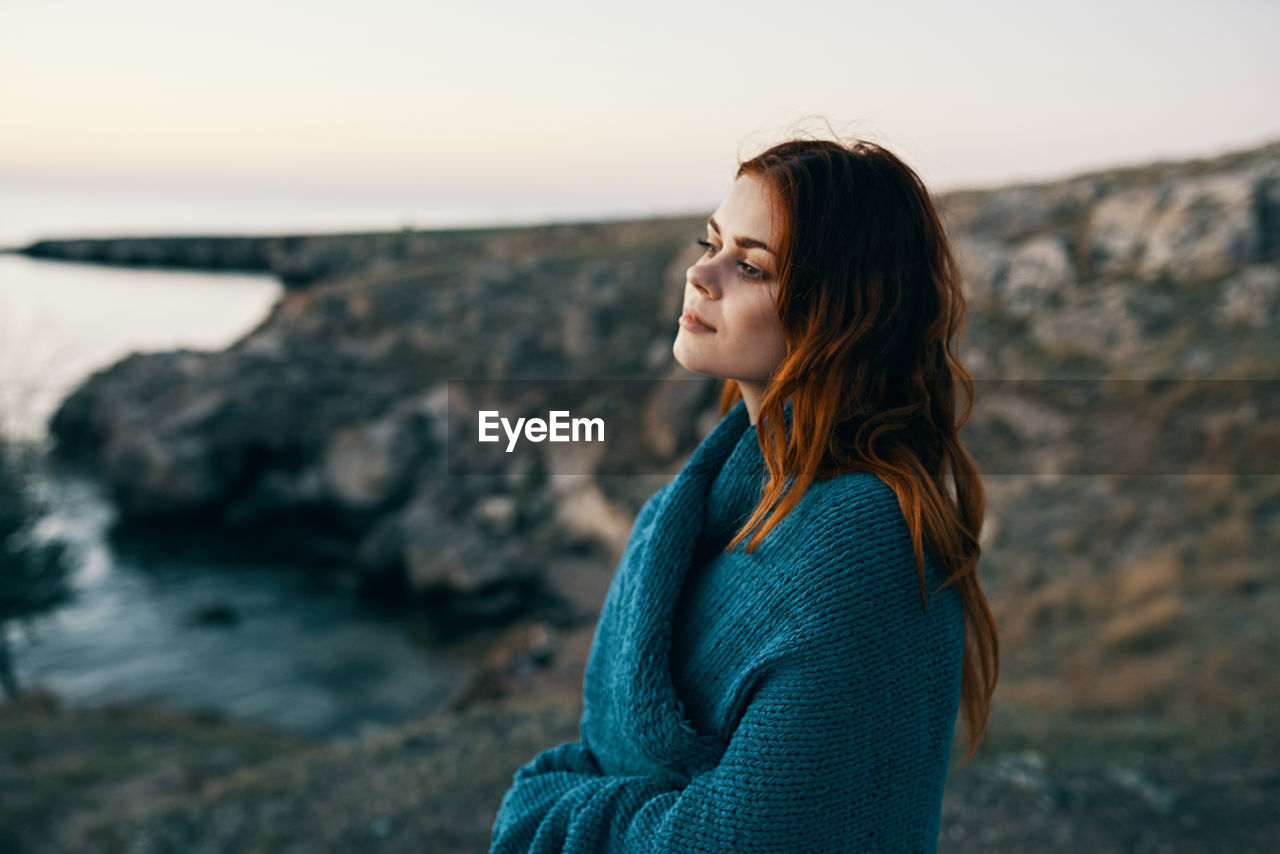 WOMAN LOOKING AWAY WHILE STANDING ON ROCK