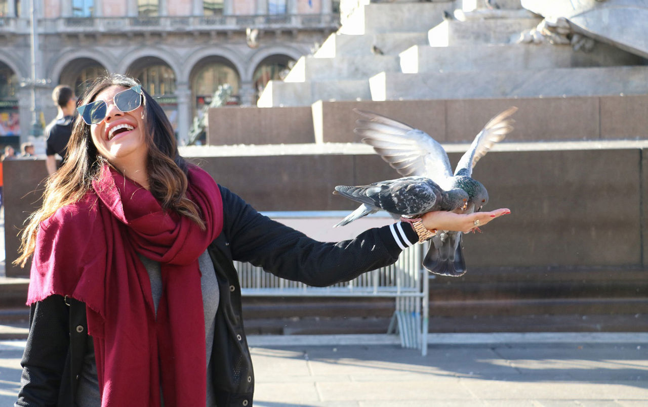 Cheerful woman feeding pigeons in city