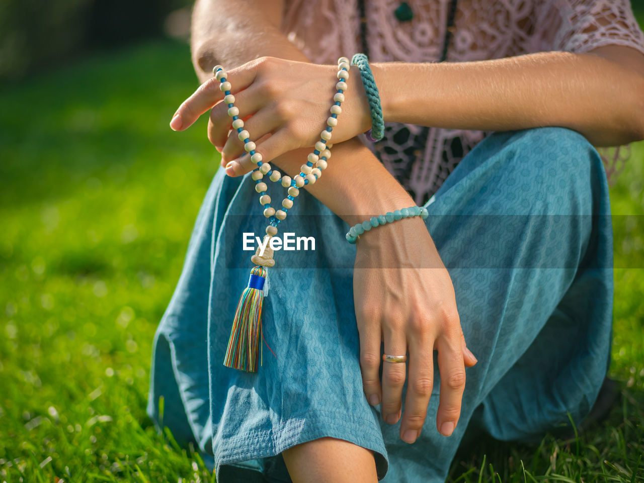 Midsection of woman with bead jewelry sitting on grassy field
