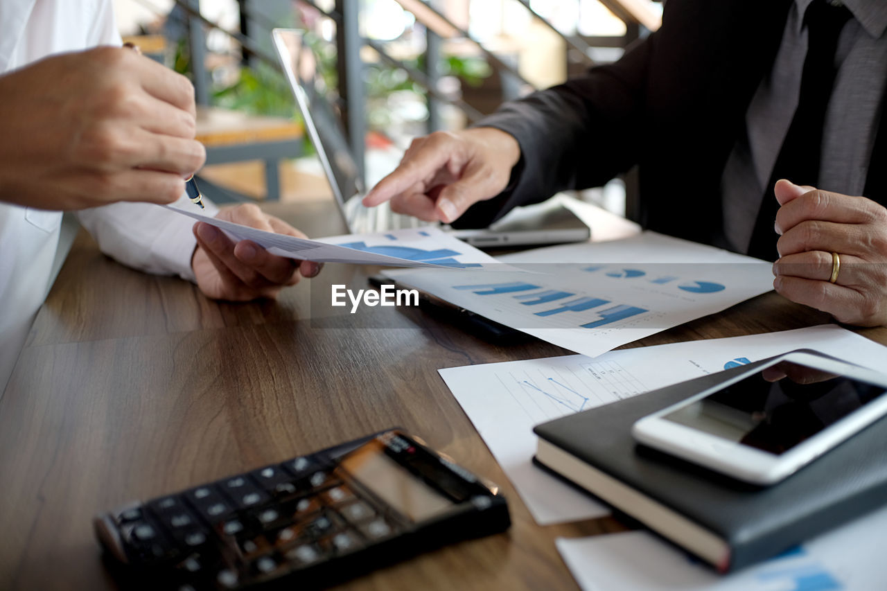 Midsection of businessman and colleague working over graph on table