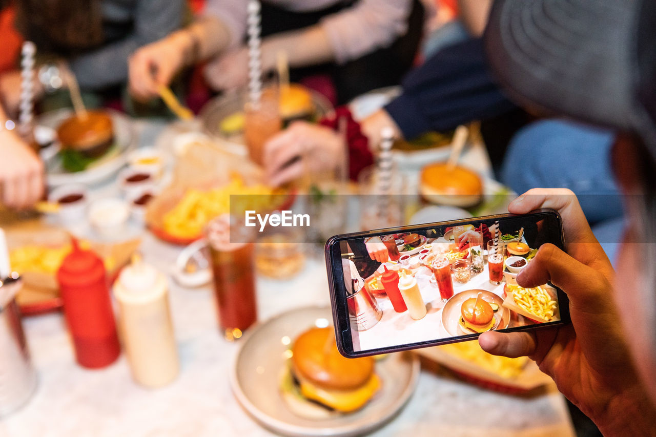 Cropped image of teenage boy photographing food and drinks served on table at restaurant