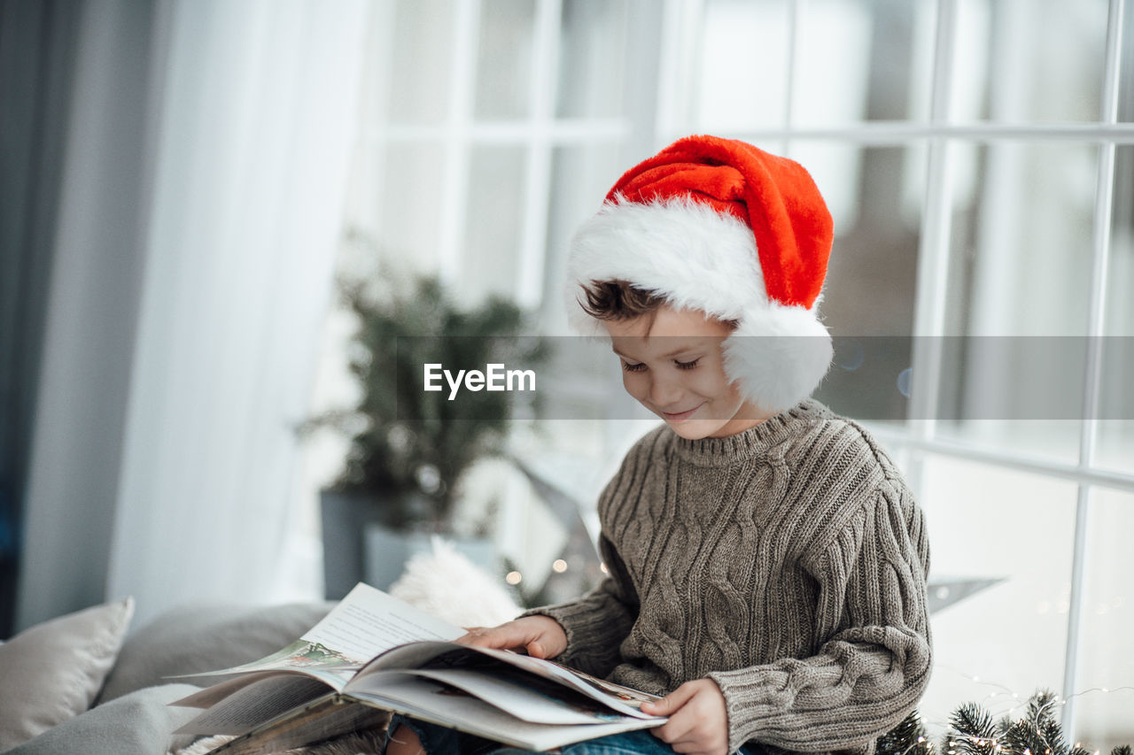 Smiling boy reading book while sitting at home