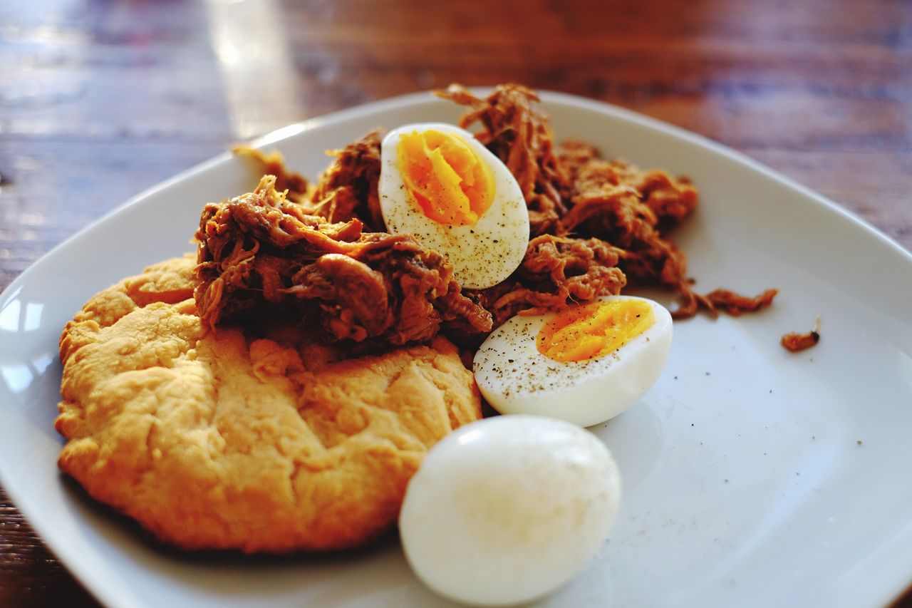 Close-up of biscuit and pulled pork with boiled eggs in plate on table