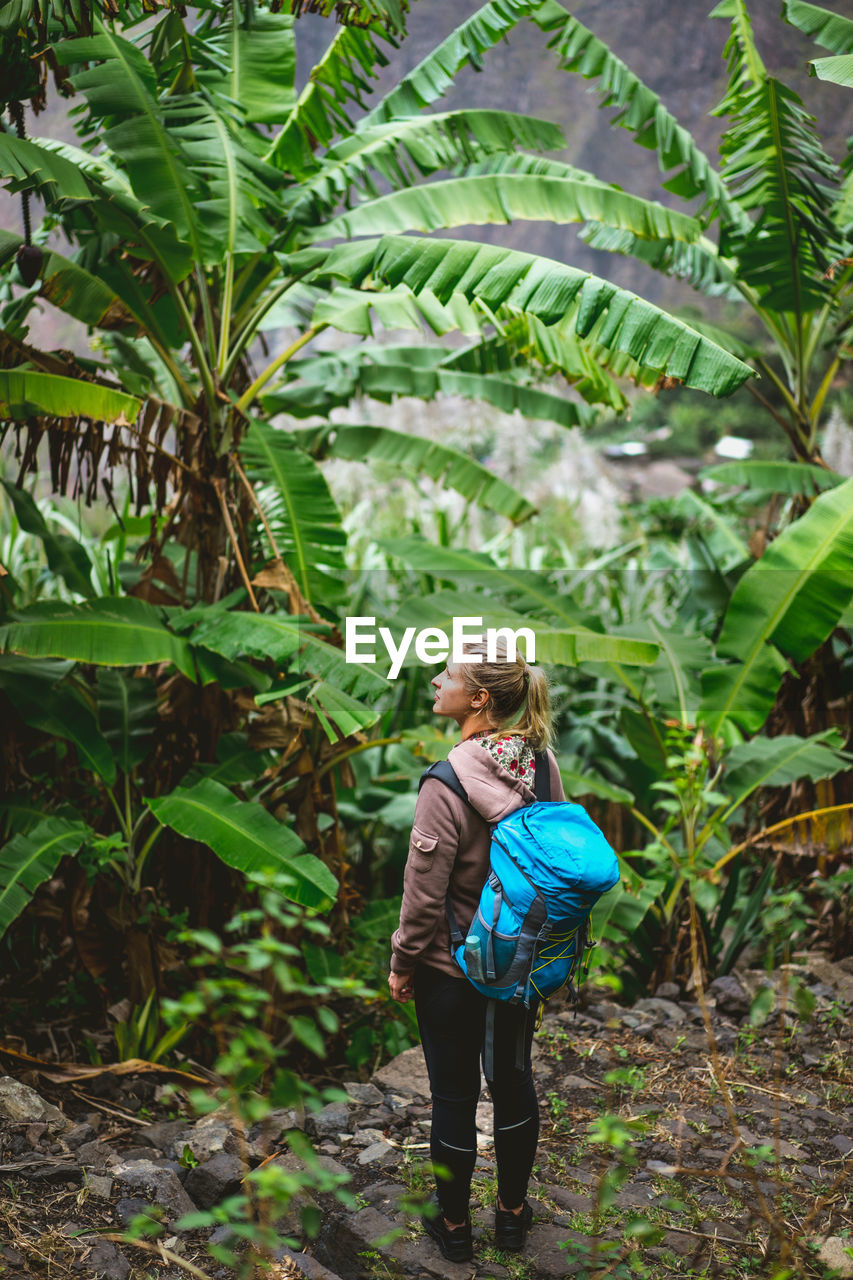 Blond young women with blue backpack admire banana. santo antao island, cape verde